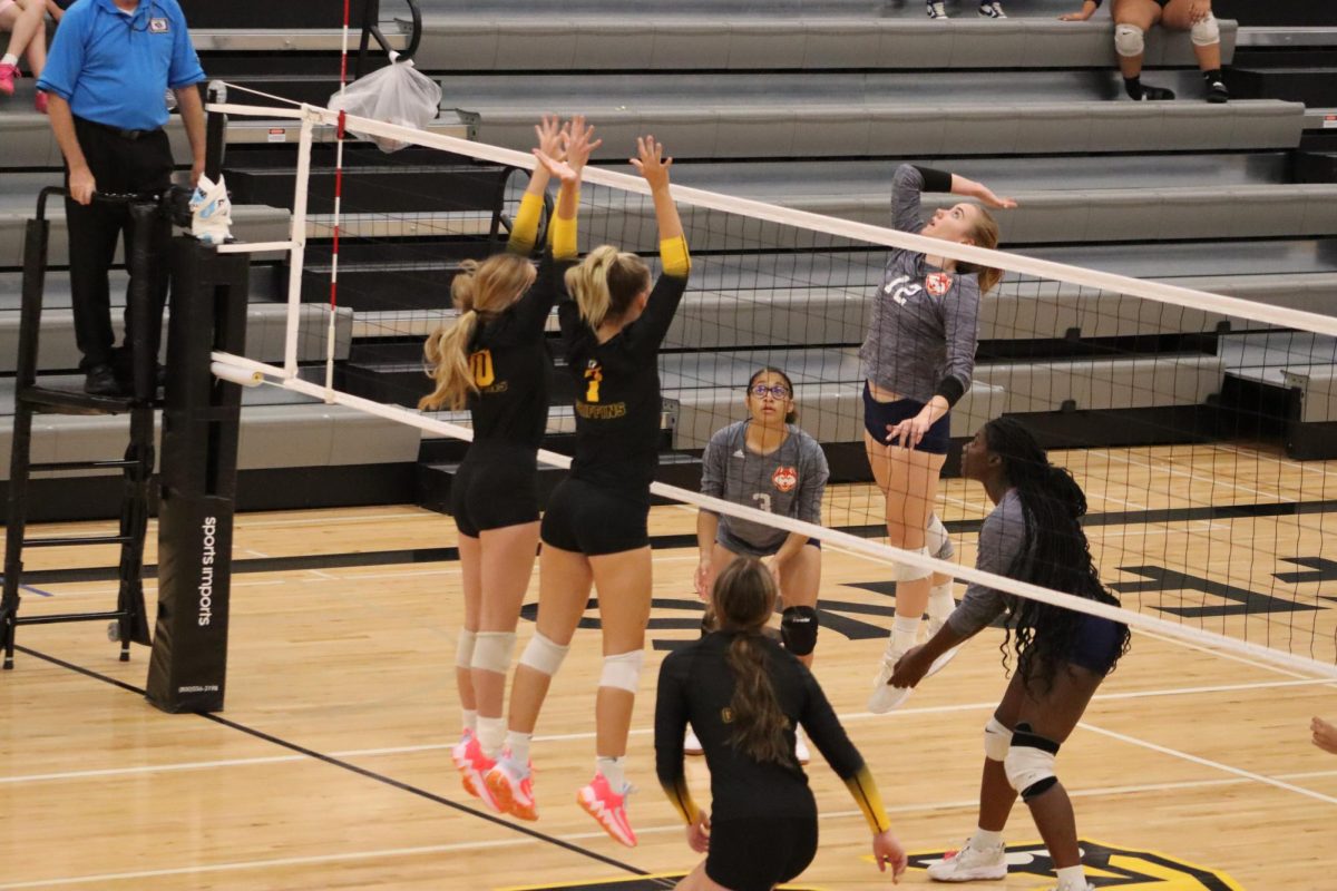 Leaping into the air, Kendra Gross (10) and Avery Kelsay (9) attempt to block the incoming ball.