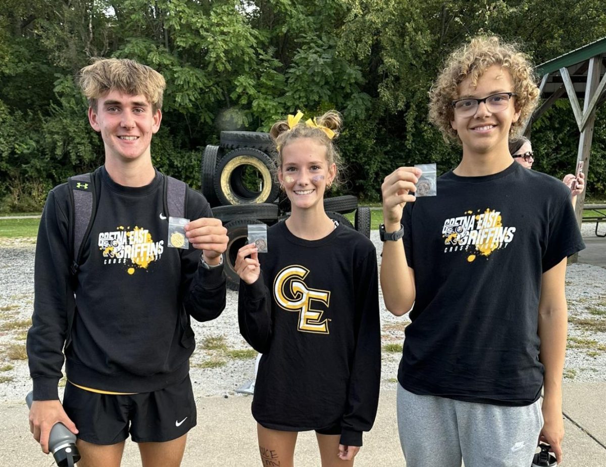 Girls cross country coach Megan Sughroue takes a picture of the state qualifiers with their medals after Districts. I am so proud of Braden, Elliot, and Evynn for being the first ever state qualifiers for cross country in Gretna East history, Sughroue said. The hard work they put in over the summer and all season paid off. They are building a strong foundation for our program to grow on in the coming years. 