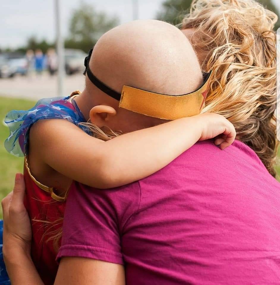 In September, 2017, six months after Ava Reinerts cancer diagnosis, Reinert hugs her mother, Amanda Reinert, at Sammys Superheroes Foundations Glow Gold event. Sammys Superheroes is another childhood cancer non-profit group who raises money for pediatric cancer research.  