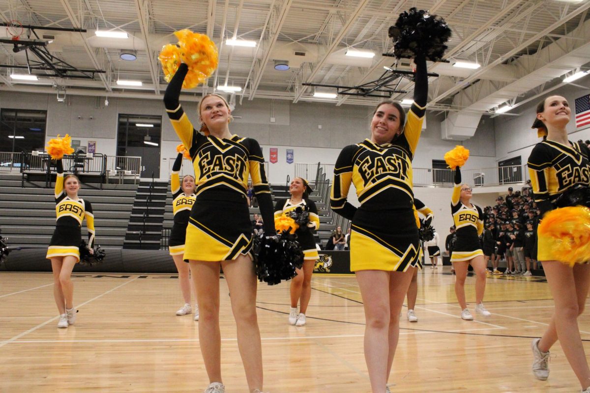 Grinning with spirit, sophomore Addi Shannon and junior Kayla Hartmann wave into the crowd of parents after the varisty cheer teams final performance at the spring pep rally.