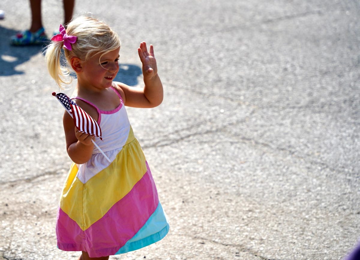 After seeing other children wave at the parade particpants, a young girl joins in. 