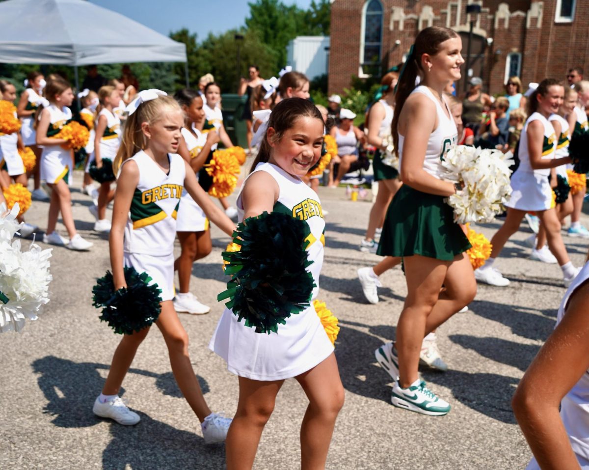 Smiling at the crowd, a junior cheerleader walks with the Gretna High School cheerleaders and other young girls. 