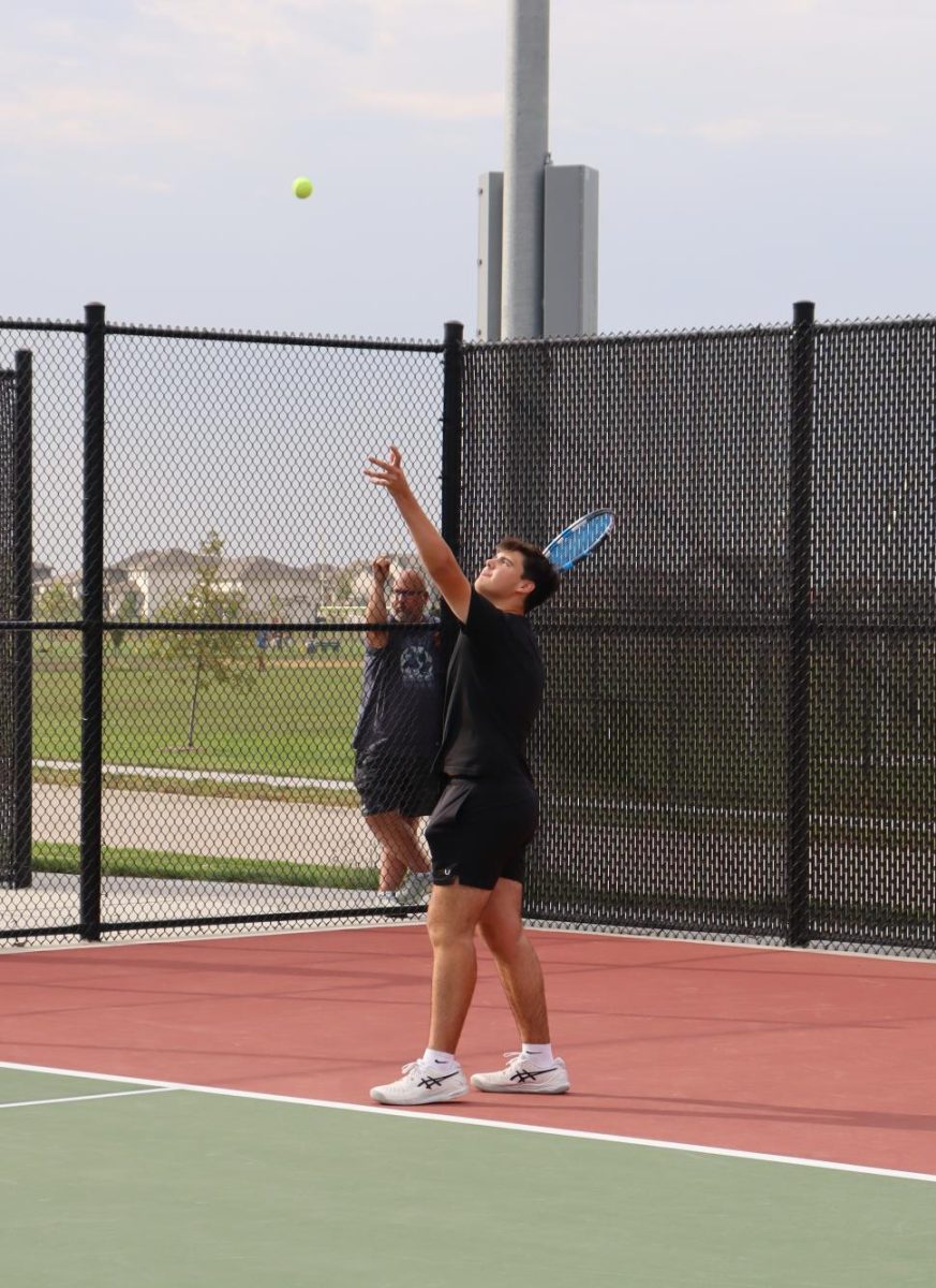 Thowing the ball up in the air before he smashes it over the net, senior Henry Hauptman sets his eyes on the ball. Hauptman won his match 8-0. 