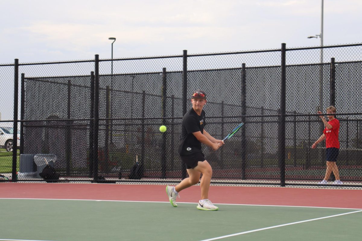 Stepping with his front, right foot, junior Ethan Boukal hits the ball underhand. Boukal won his single's match 8-0.