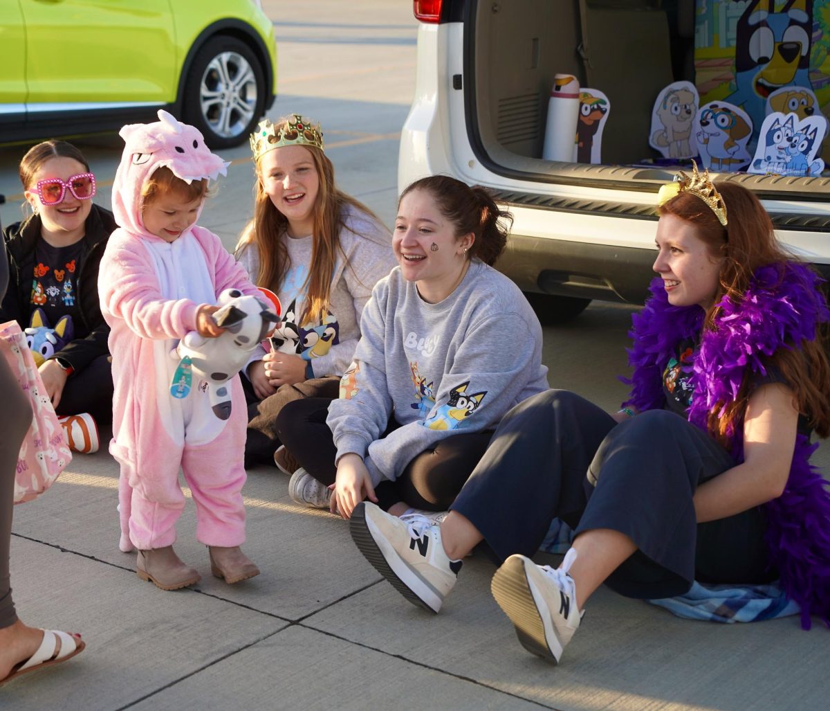 Holding onto a "Muffin" stuffed animal, a Trunk-or-Treater gets a smile from senior Ayla Meraz. Along with Ayla, seniors Kaydence Meraz and Alyssa Belitz along with junior Ava Fink had a "Bluey" themed trunk.