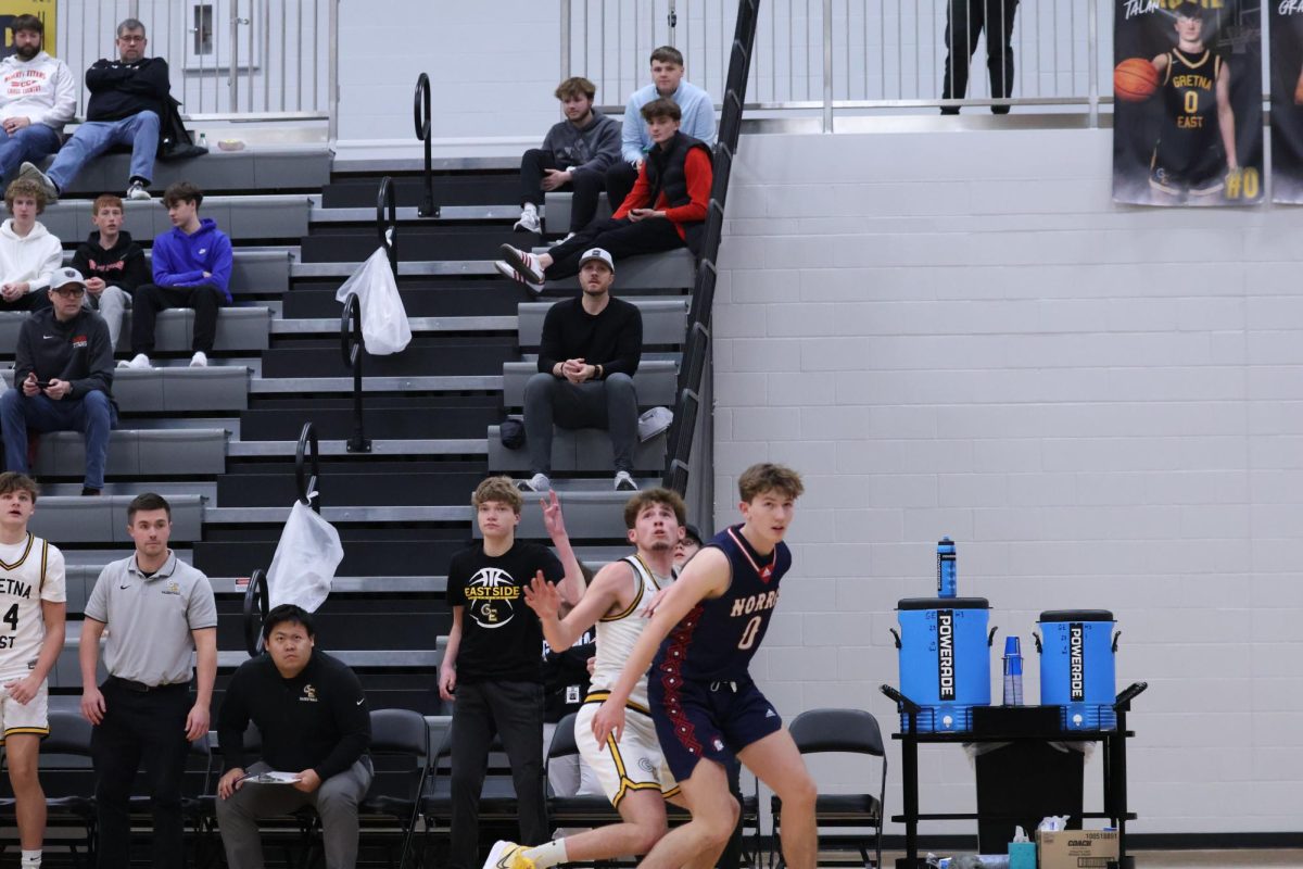 Holding the number three on his fingers, freshman Damon Dauel cheers from the bench during the boys' basketball game against Norris on January 10th. As the team manager, Damon sat courtside every game and helped encourage the team. 