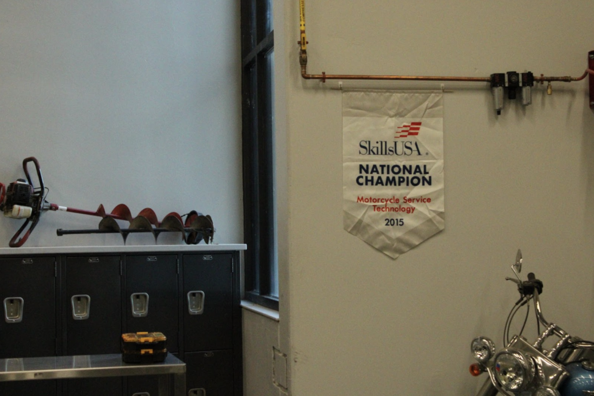 Hung up in the workshop of teacher Tim Gatewood, a banner of a national champion’s award from SkillsUSA shows one of the many categories. This was awarded for Motorcycle Service Technology, proving the niche genres one could compete in. “There are hundreds of other different competitions you could win from,” Gatewood said. (Photo by Luci Barone)
 
